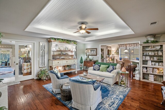 living room featuring a raised ceiling, ceiling fan, plenty of natural light, and dark wood-type flooring