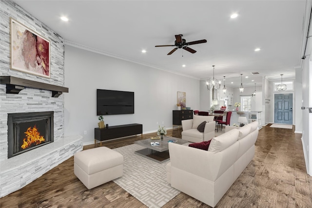 living room featuring hardwood / wood-style floors, ceiling fan with notable chandelier, a stone fireplace, and crown molding