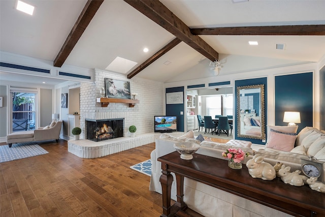 living room with wood-type flooring, vaulted ceiling with beams, a brick fireplace, and a healthy amount of sunlight