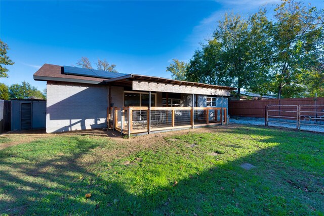 back of house featuring solar panels, a storage unit, and a lawn