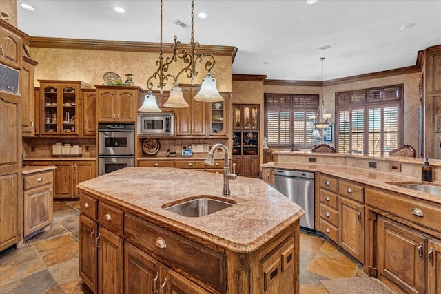 kitchen with sink, hanging light fixtures, ornamental molding, an island with sink, and stainless steel appliances