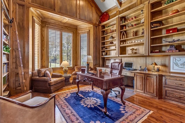 office area with built in features, wood walls, vaulted ceiling, built in desk, and light wood-type flooring