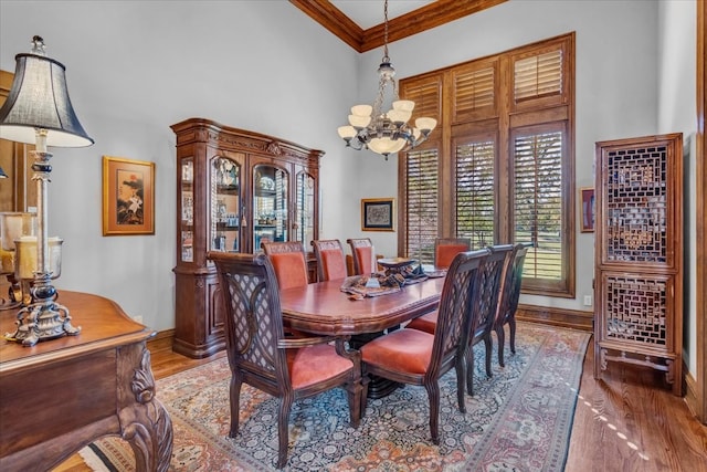 dining space with hardwood / wood-style floors, crown molding, a high ceiling, and a chandelier