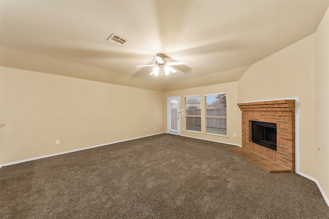 unfurnished living room with dark carpet, lofted ceiling, a brick fireplace, ceiling fan, and a textured ceiling