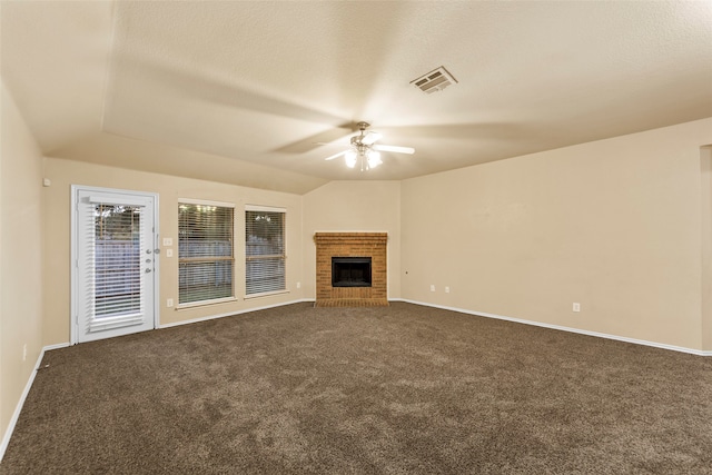 unfurnished living room with a brick fireplace, a textured ceiling, vaulted ceiling, ceiling fan, and dark colored carpet