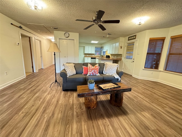 living room with ceiling fan, a textured ceiling, and light wood-type flooring