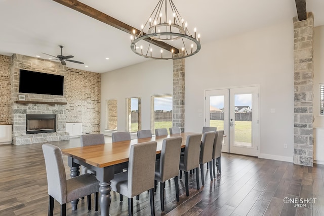 dining room with french doors, a stone fireplace, dark hardwood / wood-style floors, a towering ceiling, and ceiling fan with notable chandelier