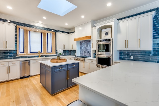 kitchen with a skylight, white cabinetry, light stone counters, crown molding, and appliances with stainless steel finishes