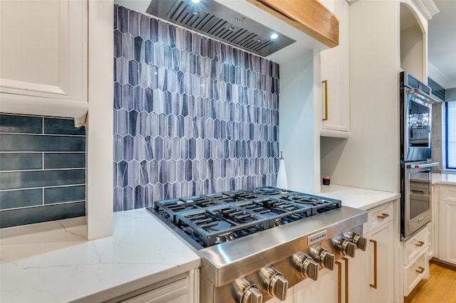 kitchen with exhaust hood, tasteful backsplash, light hardwood / wood-style flooring, and light stone counters