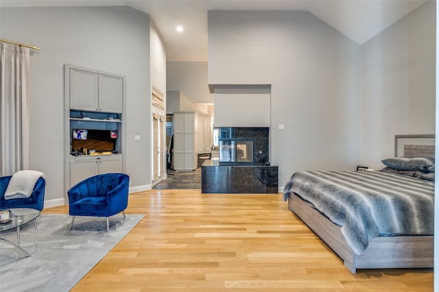 bedroom featuring a tile fireplace, hardwood / wood-style flooring, and high vaulted ceiling