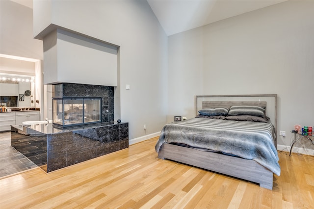 bedroom with a tile fireplace, hardwood / wood-style flooring, and high vaulted ceiling