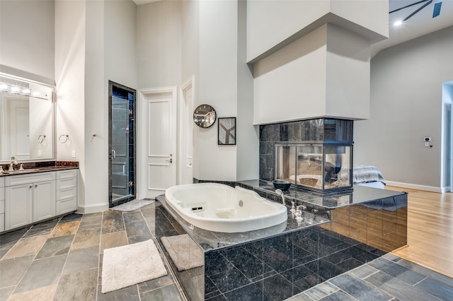 bathroom featuring vanity, a tile fireplace, hardwood / wood-style flooring, separate shower and tub, and a towering ceiling