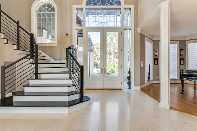 foyer entrance with ornate columns, french doors, a towering ceiling, light hardwood / wood-style floors, and ornamental molding