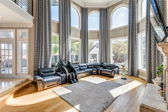 living room with wood-type flooring, a towering ceiling, plenty of natural light, and ornamental molding