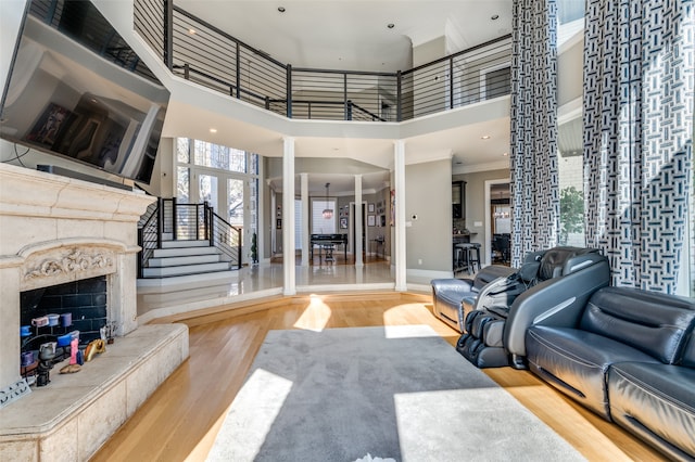 living room featuring ornate columns, a premium fireplace, crown molding, a towering ceiling, and hardwood / wood-style flooring