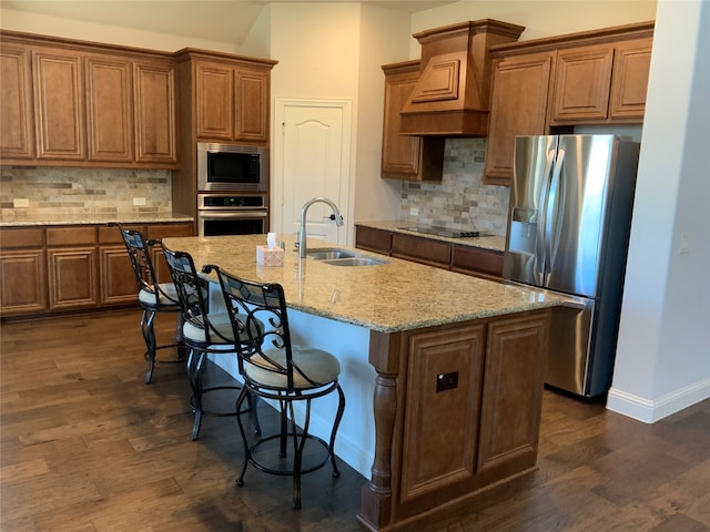 kitchen with appliances with stainless steel finishes, tasteful backsplash, dark wood-type flooring, sink, and an island with sink