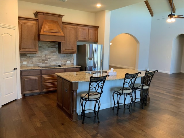 kitchen with dark wood-type flooring, a kitchen breakfast bar, stainless steel refrigerator with ice dispenser, an island with sink, and custom exhaust hood