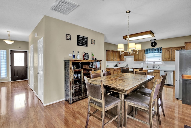 dining space with a textured ceiling, a notable chandelier, sink, and light hardwood / wood-style flooring