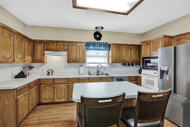 kitchen with sink, appliances with stainless steel finishes, tasteful backsplash, light hardwood / wood-style floors, and a kitchen bar