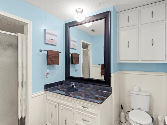 bathroom with vanity, a textured ceiling, toilet, and walk in shower