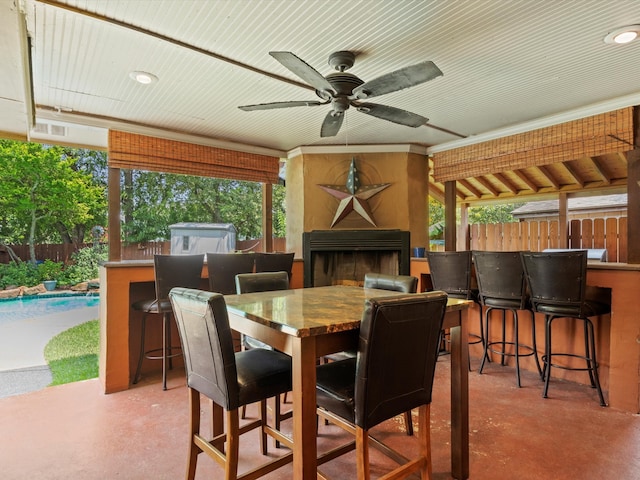 dining space with concrete flooring, exterior fireplace, a healthy amount of sunlight, and ceiling fan