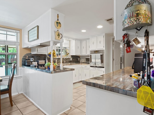 kitchen with backsplash, white cabinets, oven, light tile patterned flooring, and kitchen peninsula