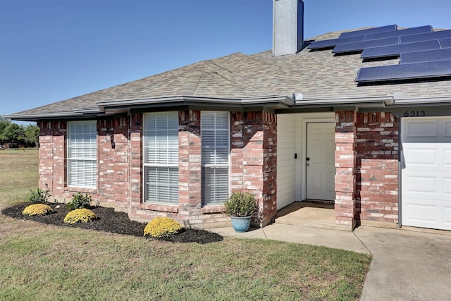 doorway to property with solar panels, a garage, and a lawn