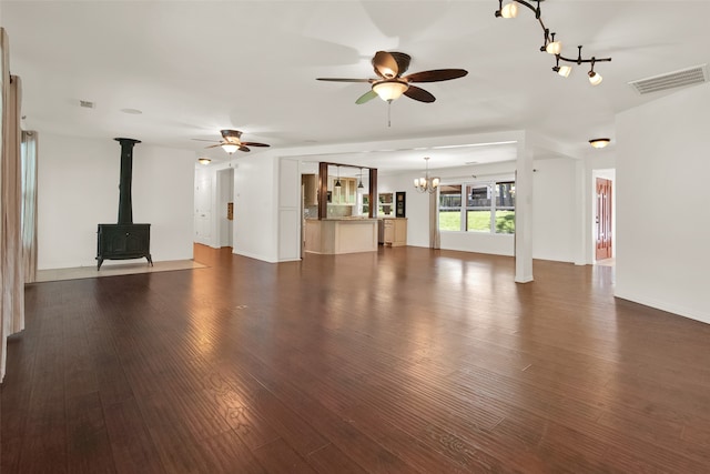 unfurnished living room featuring a wood stove, dark hardwood / wood-style flooring, and ceiling fan with notable chandelier