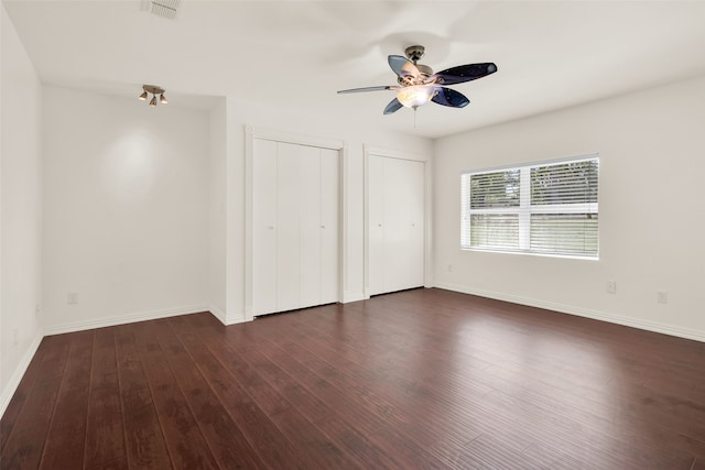 unfurnished bedroom with multiple closets, ceiling fan, and dark wood-type flooring