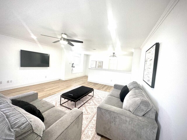 living room featuring ceiling fan, ornamental molding, a textured ceiling, and light wood-type flooring