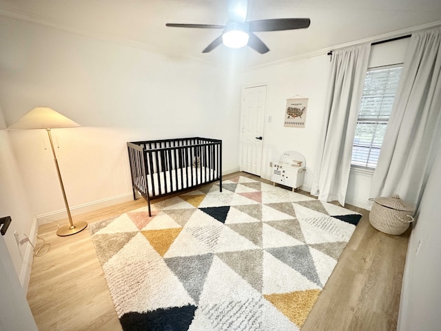 bedroom with hardwood / wood-style floors, a nursery area, ornamental molding, and ceiling fan