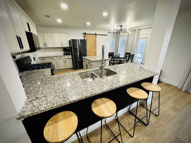 kitchen with white cabinetry, light stone countertops, sink, a barn door, and black appliances