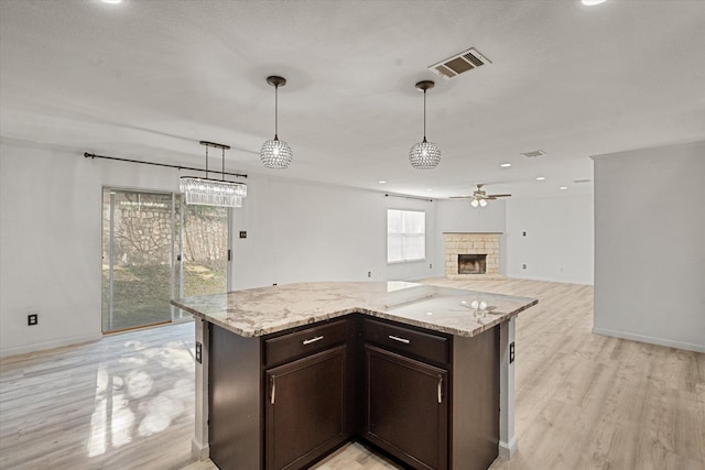 kitchen with light stone counters, dark brown cabinets, black appliances, light hardwood / wood-style flooring, and hanging light fixtures