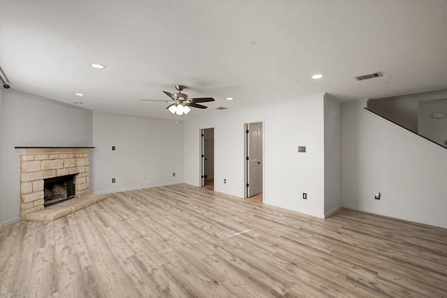 unfurnished living room featuring a stone fireplace, ceiling fan, and light hardwood / wood-style floors