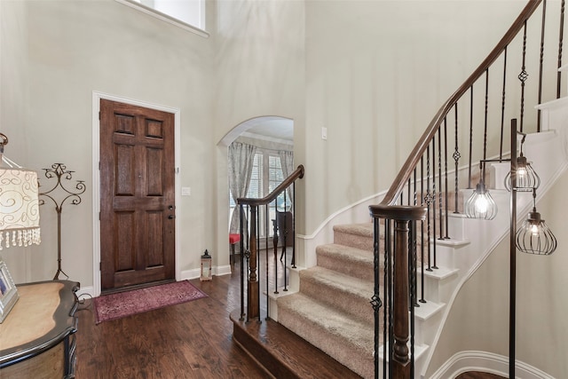 foyer featuring baseboards, arched walkways, a towering ceiling, dark wood-type flooring, and stairs