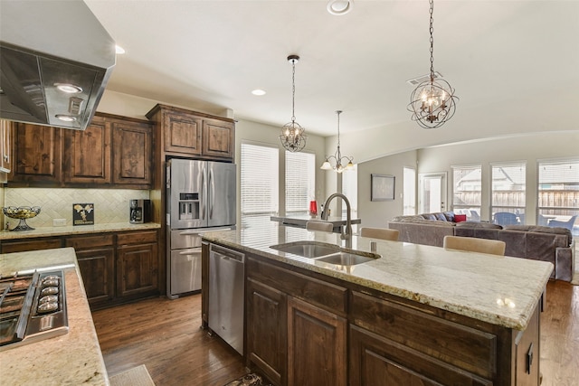 kitchen with a center island with sink, appliances with stainless steel finishes, open floor plan, a sink, and extractor fan