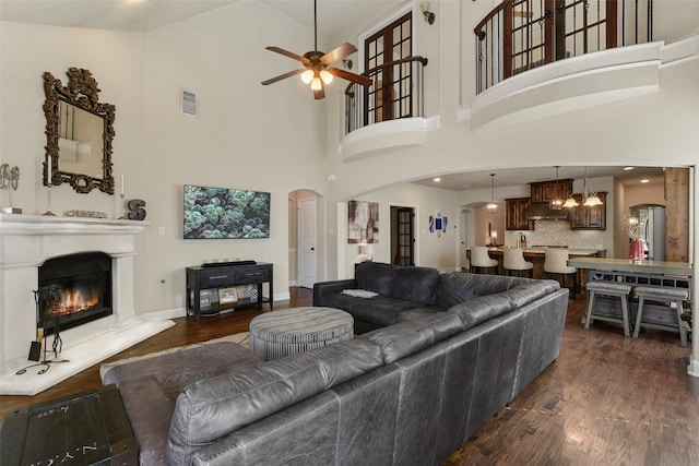 living room featuring dark wood-type flooring, arched walkways, visible vents, and a glass covered fireplace