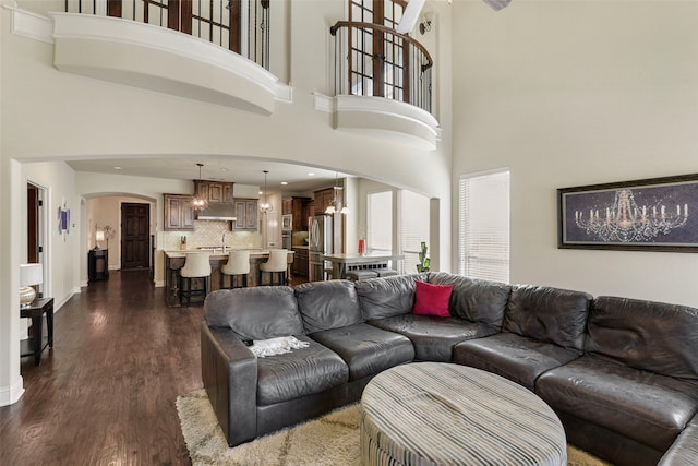 living room with arched walkways, dark wood-type flooring, baseboards, and a notable chandelier