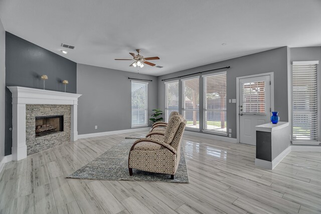 living room featuring light hardwood / wood-style flooring, ceiling fan, and a stone fireplace