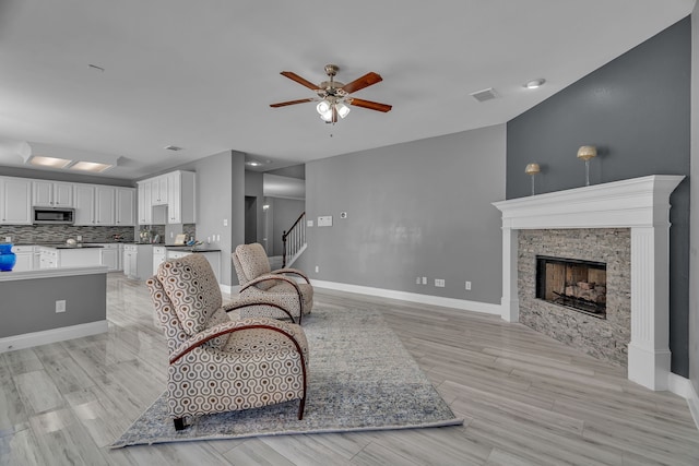 living room with a fireplace, light wood-type flooring, and ceiling fan