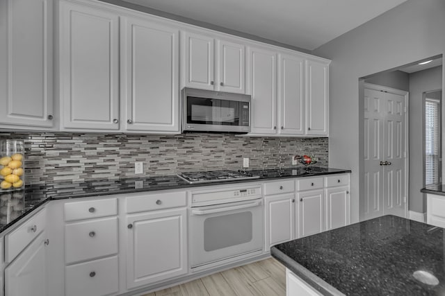 kitchen with white cabinetry, stainless steel appliances, dark stone countertops, decorative backsplash, and light wood-type flooring