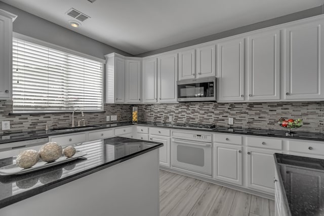 kitchen with appliances with stainless steel finishes, backsplash, sink, dark stone countertops, and white cabinetry