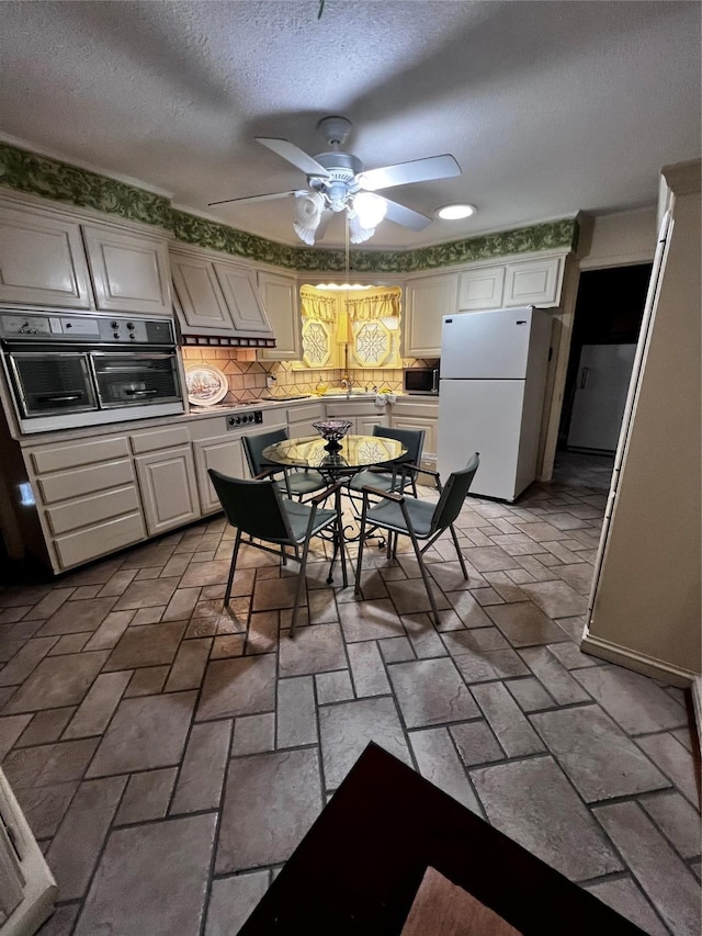 kitchen with oven, ceiling fan, a textured ceiling, tasteful backsplash, and white fridge