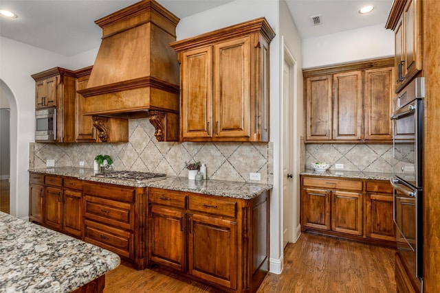 kitchen featuring arched walkways, dark wood finished floors, visible vents, appliances with stainless steel finishes, and premium range hood