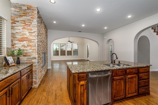 kitchen featuring a sink, open floor plan, light wood-type flooring, light stone countertops, and dishwasher