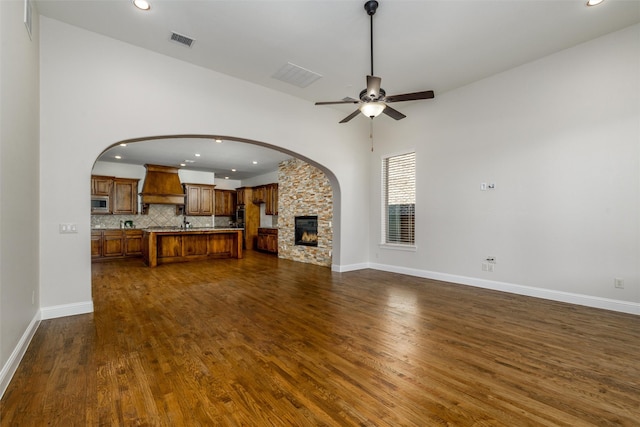 unfurnished living room featuring dark wood-style floors, a fireplace, visible vents, ceiling fan, and baseboards