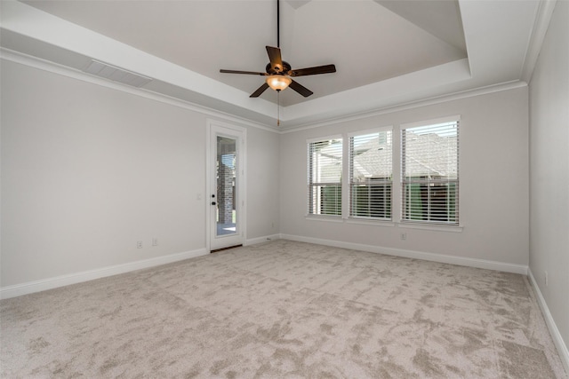 empty room featuring carpet floors, ornamental molding, a raised ceiling, and baseboards