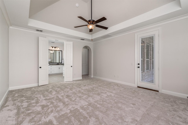 unfurnished bedroom featuring arched walkways, light carpet, baseboards, access to exterior, and a raised ceiling