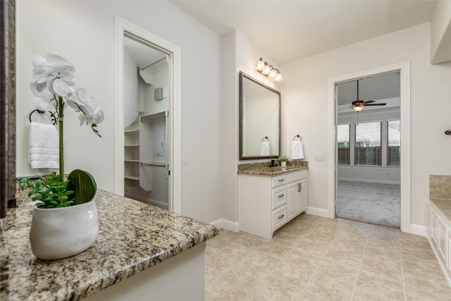 bathroom featuring a walk in closet, two vanities, baseboards, and tile patterned floors