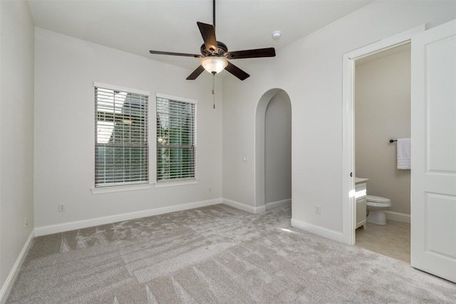 unfurnished bedroom with arched walkways, baseboards, ensuite bath, ceiling fan, and carpet